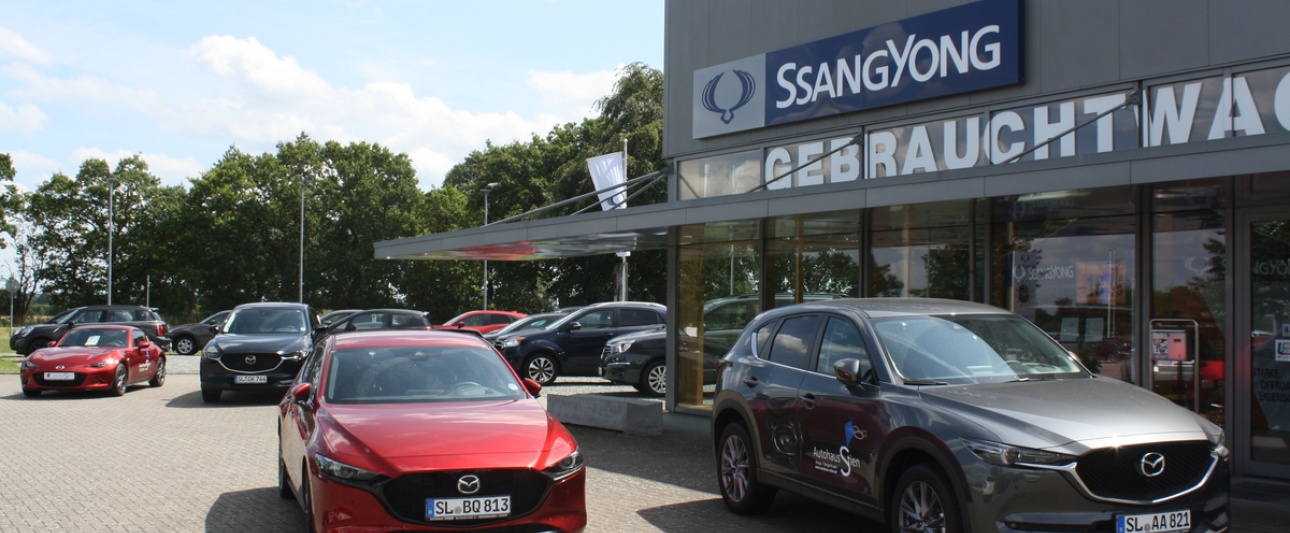 Fahrzeuge vor einem Autohaus mit Ssangyong-Werbung